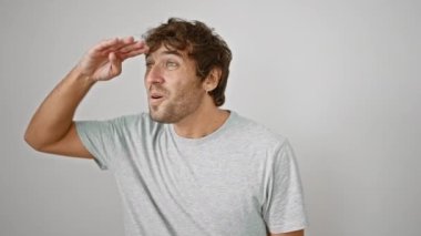 Mutlu genç bir adam, sıradan tişörtüyle gülümsüyor, uzak manzaraya bakarken ellerini koruyor. beyaz arkaplanda izole edilmiş.