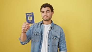 Kendine güvenen genç bir Arap, elinde emirlik pasaportu, parlak sarı izole bir arka planda başarı diye haykıran ciddi bir ifadeyle seni işaret ediyor..