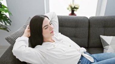 Genç bir İspanyol kadın evdeki gri bir kanepede dinleniyor, huzur ve memnuniyet saçıyor..