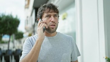 Yakışıklı, genç bir adamın portresi, telefonunda konuşan sarışın sakallı, yoğun bir şekilde. Şehir sokaklarında konuşurken yakalandı. Yüzünde ciddi ama rahat bir ifade var..
