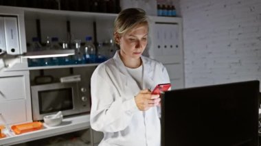 Modern bir laboratuvar ortamında akıllı telefon kullanan odaklanmış bir kadın bilim adamı..