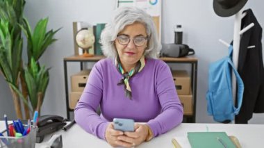 Ofiste akıllı telefon kullanan gülümseyen bir kadın profesyonellik yayar ve kolaylık sağlar..