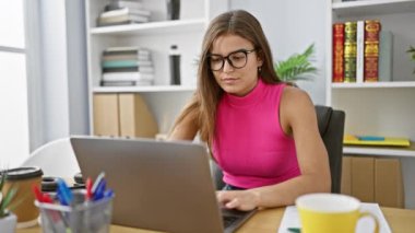 Ofiste dizüstü bilgisayarda çalışan aşırı çalışkan ve stresli genç bir kadın, mutsuz bir yöneticinin portresi.