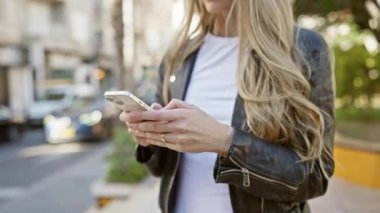 Güneşli bir günde şehirde akıllı telefon kullanan sarışın bir kadın..