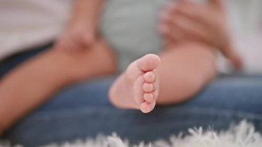 Sevgi dolu anne, sıcak bir oturma odasında kanepede oturuyor, küçük kızının ayaklarına hafifçe dokunuyor ve birlikte samimi bir an yaşıyor.
