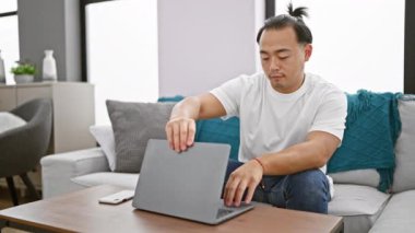 Neşeli genç Çinli adam online oturumunu bitiriyor, bilgisayarını tatmin olmuş bir gülümsemeyle kapatıyor, evdeki oturma odasındaki kanepede oturuyor.