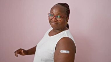 Kendine güvenen Afro-Amerikalı kadın, başparmak yukarı tamam işareti, yara bandı kaplı kol, canlı pembe izole geçmiş