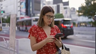 Tokyo 'da gözlüklü güzel İspanyol kadın. Şehir sokaklarında akıllı telefon aracılığıyla dijital bağlantı.
