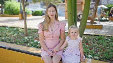 Kendinden emin bir şekilde gülümseyen beyaz anne ve kız parktaki bankta oturup eğlenmenin tadını çıkarıyorlar.