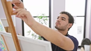 Kulaklıklı bir adam, bir sanat stüdyosundaki tuvale resim yapar, yaratıcılığı ve konsantrasyonu somutlaştırır..