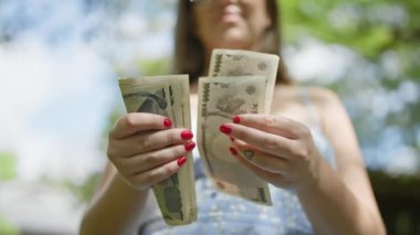 Tutumlu genç bir kadın, geleneksel Japon parkının yemyeşil yeşili arasında, finansal özgürlüğünü pekiştiren bir yığın yeni banknot sayıyor.