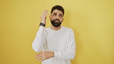 Düşünceli genç bir adam, düşünceli bir yüz, şüphe içinde duruyor, eli çenesinde, bir soruyu çözmeye çalışıyor. Sarı arka planda izole edilmiş, yüzünde bir gülümseme var..