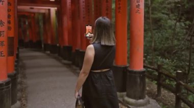 Gözlüklü göz kamaştırıcı İspanyol kız Japonya 'nın fushimi torii kapılarını yakalıyor. Kültüre dalmış, akıllı telefonunun canlı turuncu mimarisini çekiyordu..