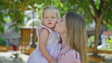 Neşeli anne sarılıyor, kollarında sevgilisiyle dışarıda yeşil parkta kızını öpüyor.