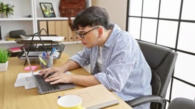 Modern bir ofis ortamında dizüstü bilgisayarla çalışırken boynu ağrıyan gözlüklü bir genç.