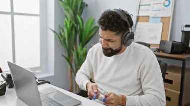 Kulaklık takan sakallı genç bir adam modern ofis ortamında dolma kalemle but gibi oynuyor..