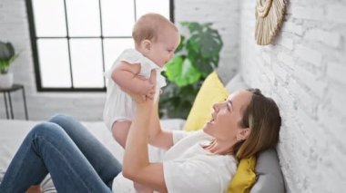 Gülümseyen anne yatakta oturuyor, mutlu bir şekilde kızını kucağında tutuyor, sıcak bir yatak odasında oyun oynamanın tadını çıkarıyor.