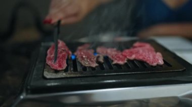 Modern yemek deneyimi, genç bir kadının elleri Japon restoranında ızgarada lezzetli wagyu bifteği pişiriyor, lezzetli kızarmış etin tadını çıkarıyor.