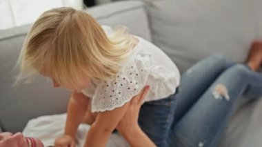 Kafkasyalı anne ve kız kanepede rahat bir şekilde uzanıp evlerinin sıcaklığında oynayıp gülümsüyorlar.