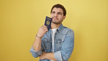 Ciddi genç Arap bir adam, eli çenesinde, kompleks fikirler üzerinde kafa yoruyor, emirlik pasaportu taşıyor. Sarı arka planda izole edilmiş, yüzü düşünceli bir kafa karışıklığını temsil ediyor, cevaplar arıyor..