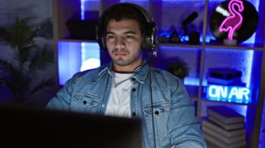 Geceleri oyun odasında kulaklıkları olan genç bir adam neon ışıklarla aydınlatılıyor..