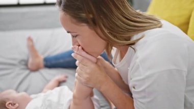 Neşeli anne ve kız, sıcak yatak odalarında, yatakta otururken ayaklarının altında komik bir öpücük paylaşırlar.