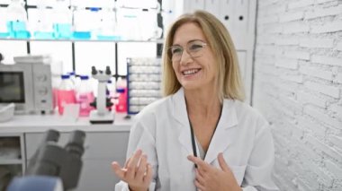 Kendine güvenen orta yaşlı sarışın bilim adamı, gülüyor ve başka tarafa bakıyor, laboratuvarında doğal bir gülümseme sergiliyor..