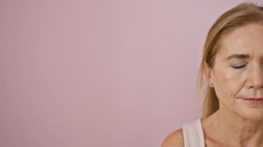 Sarı saçlı, gülümseyen orta yaşlı bir kadının portresi pembe bir duvara yaslanmış, olgun güzelliğini ve duruşunu yakalıyor..