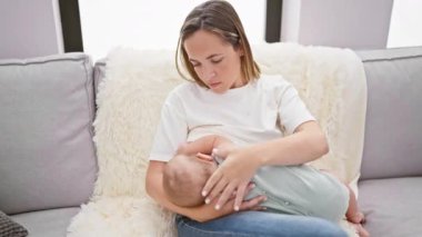 Evde sevgi dolu bir anne, sevgi dolu bir aile kanepesinde oturuyor, bebeğini emziriyor, bu samimi annelik anının tadını çıkarıyor, bebeğe besleyici anne sütü sunuyor.