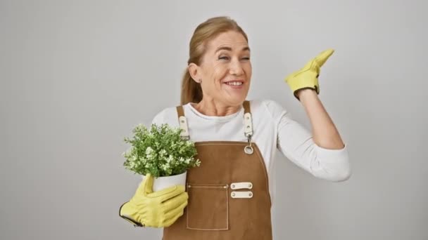 喜ばしい中年のブロンドの女性は勝利で花屋 自信を持って植物の鍋を保持し 彼女の勝利の表情と祝賀笑顔は 幸福と成功を除いて 白い背景に孤立しました — ストック動画