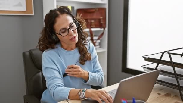 疲れた中年のヒスパニック系女性は ノートパソコンでヘッドフォンをオフィスの机に取り除き 仕事の日に疲労を示しました — ストック動画