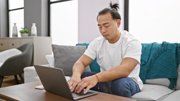 強調された若い中国人男性は ノートパソコンに集中し ソファーで自宅で指なしで言った — ストック動画