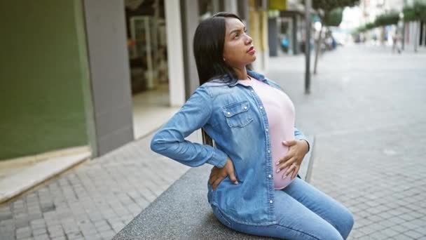 疲れた若い妊婦 彼女の腹に触れる 都市のストリートベンチで熟考に座って リラックス 期待される母性の感情のバランスをとり 産婦人科の痛み — ストック動画