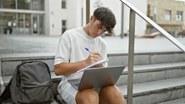 在大学的楼梯上 冷静而恐慌的年轻人放松了下来 认真地专注于在笔记本电脑上记笔记 — 图库视频影像