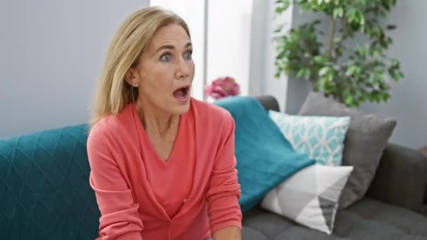 Erstaunte Blonde Frau Mittleren Alters Die Ungläubig Auf Dem Sofa — Stockvideo