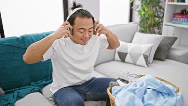 Молодой Китаец Слушает Музыку Держа Дома Одежду Корзины — стоковое видео