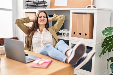 Young beautiful hispanic woman business worker relaxed with hands on head at office