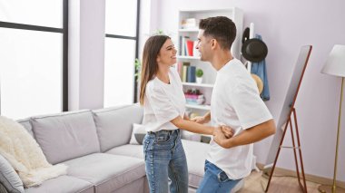 Neşeli bir kadın ve erkek, aydınlık, rahat bir oturma odasında birlikte dans ediyor, bir neşe ve birliktelik hissi tasvir ediyor..