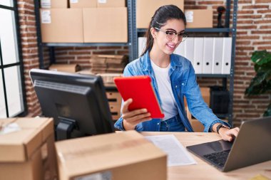 Young beautiful hispanic woman ecommerce business worker using touchpad and laptop at office