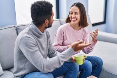 Man and woman couple sitting on sofa drinking coffee at home