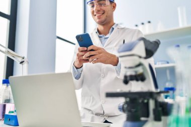 Young hispanic man scientist smiling confident using smartphone at laboratory
