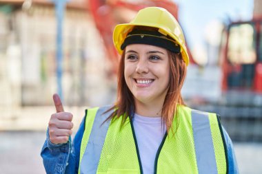 Young beautiful plus size woman architect smiling confident doing ok gesture with thumb up at street