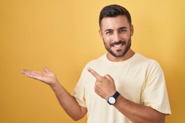 Sarı zemin üzerinde duran yakışıklı İspanyol adam hayrete düştü ve kameraya gülümsüyor.. 