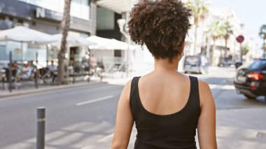 Gündüz vakti şehir caddesinde yürüyen kıvırcık saçlı, çekici, İspanyol bir kadının arka görüntüsü..