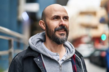 Genç kel adam gülümsüyor. Kendinden emin bir şekilde caddeye bakıyor.