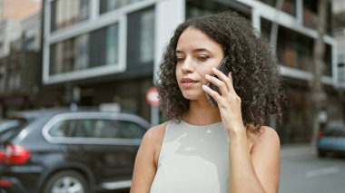 Genç ve güzel İspanyol bir kadın akıllı telefonda konuşuyor. Sokakta ciddi bir ifadeyle.