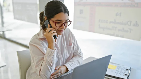 ヒスパニックの女性は 現代のオフィスの設定で電話で会話します デスク上のラップトップとクリップボード — ストック写真