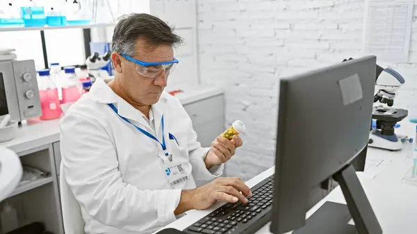 Зрелый Человек Лабораторном Халате Изучает Пузырек Лекарствами Яркой Лаборатории Компьютером — стоковое фото