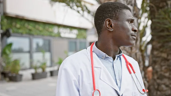在城市室外背景下身穿红色听诊器的身穿白色实验室外套的专注的非洲男子的画像 — 图库照片