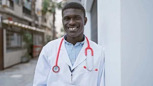 身穿白色实验室外套 带着红色听诊器的非洲男子在城市街道上微笑 — 图库照片